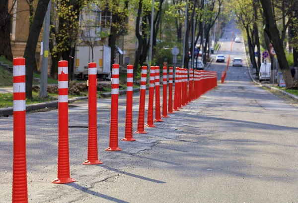 La vecchia strada con scarsa copertura asfaltata è divisa da colonne stradali rosse su una strada cittadina alla luce del sole. . — Foto Stock