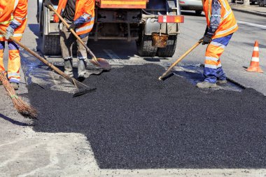 Çalışma ekibi yol tamir ederken elle kürek ile sıcak asfalt pürüzsüzler.