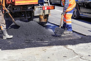 The working crew evenly distributes hot asphalt with shovels manually on the repaired site of the road. clipart