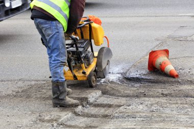 İşçi yol inşaatı sırasında bir benzin kesici ile kötü asfalt bir parça keser.