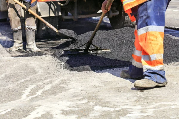 El equipo de trabajo distribuye uniformemente el asfalto caliente con una pala y un nivel de madera manualmente sobre el tramo de carretera reparado . — Foto de Stock