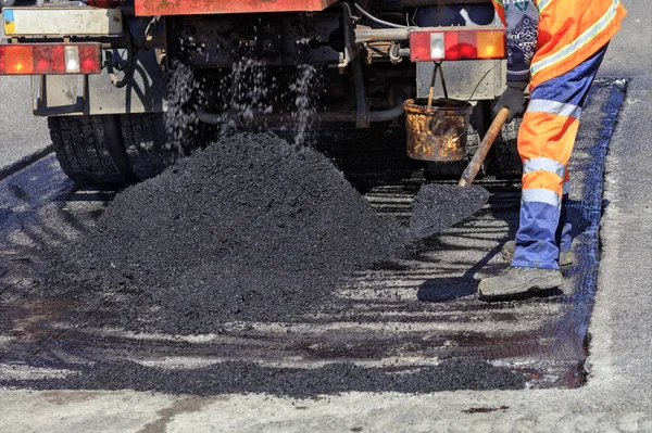 Trabajador de servicio de carretera rasbrasyvaet parte del asfalto con una pala para parchear la carretera — Foto de Stock