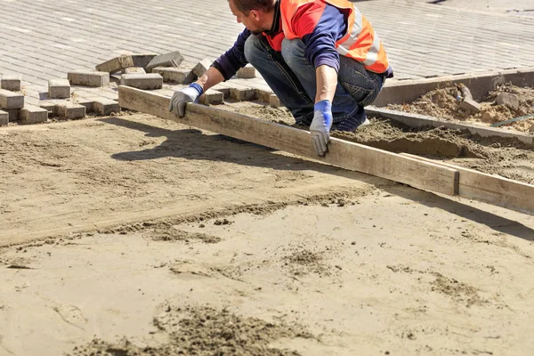 İşçi kaldırımda kaldırım döşeme için ahşap bir tahta ile kum tabanı hizalar. — Stok fotoğraf