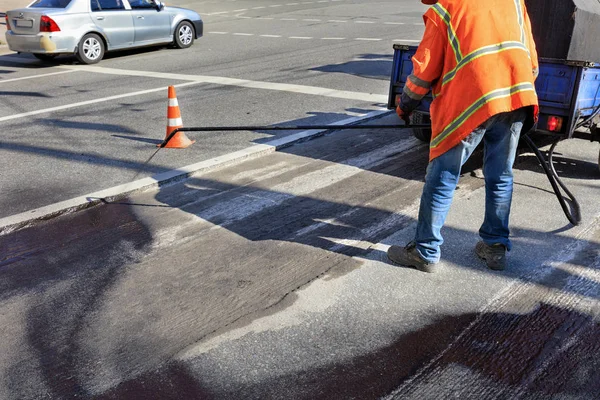 El trabajador rocía betún sobre la superficie del asfalto. Reparación parcial de la carretera asfaltada . — Foto de Stock
