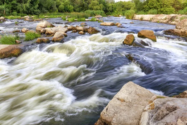 The rapid flow of the river in the blur, rocky shores, boulders and rapids, bright green vegetation on the other side of the shore. — Stock Photo, Image