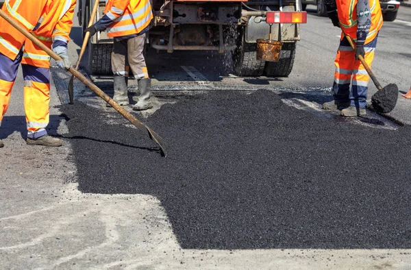 Zespół roboczy wygładza ręcznie gorący asfalt z łopatkami podczas naprawy drogi. — Zdjęcie stockowe