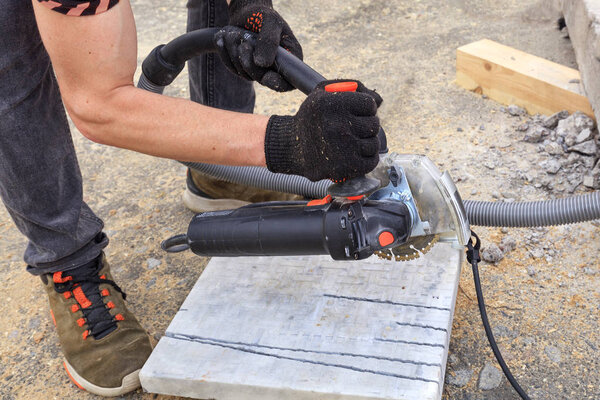 The worker cuts a metal plate and paving slabs for laying on the terrace with an angle grinder.