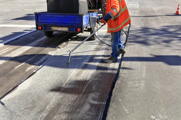 Trabajador repara parte de la carretera de asfalto, rociando betún sobre la superficie de asfalto . — Foto de Stock