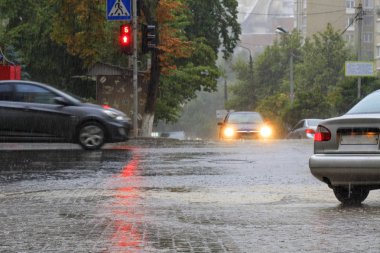 Kaldırım ve asfalt yolda ağır yağmur kırmızı bir trafik ışığı ile aydınlatılır.