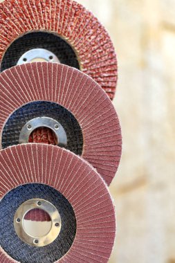 Flap grinding wheels from different grains on wood and metal one on top of another vertical on a light beige background in unsharpness. clipart