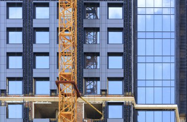 Yapım aşamasında modern bir beton binanın yakınında cephe ve vinç.