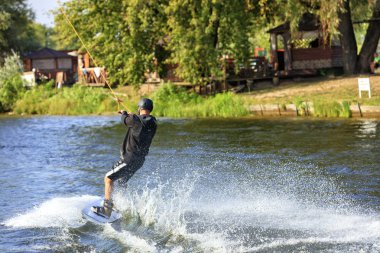 Bir wakeboarder nehrin yeşil kıyısında yüksek hızda su üzerinden acele.