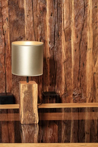 Stylish reading lamp and an old cracked wooden wall reflect on a polished wooden surface.