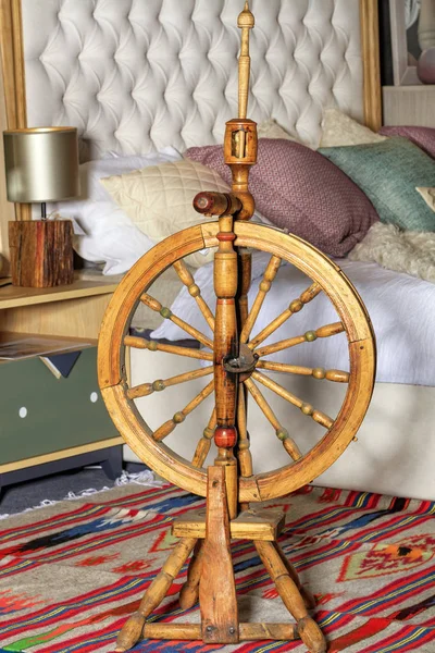 An antique spinning wheel stands on a homespun carpet at the head of the bed.