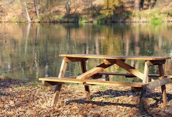 Wooden table with picnic benches in the open air on the background of fallen oak leaves near a forest lake.