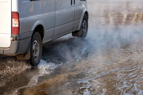 An accident on a heating main, a break in a pipe with hot water, a car driving along a flooded road, water vapor forms a smokescreen on the asphalt, an image with copy space.