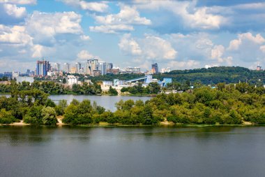 Kiev 'in sağ kıyısında Dinyeper nehri ve önlerinde adalar olan bir şehir ve sıcak bir yaz gününde ufukta yüksek binaları olan yeni bir yerleşim alanı manzarası..