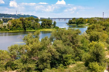 Dnipro Nehri 'ndeki pitoresk adalar ağaçlar ve yeşil otlarla kaplıdır. Nehir üzerindeki köprülerin ve Kyiv tepelerinin manzarası.