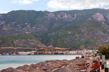 Korint Körfezi 'nin ıssız kıyılarında güneşli şezlongların bulunduğu plaj şemsiyelerinin tepeleri, Yunanistan' ın uyanış şehri Loutraki 'nin sabah renklerinin ve bulanık dağ sıralarının arkaplanlarına karşı..