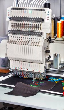 Çeşitli kumaş ve derilere nakış işlemek için modern profesyonel nakış makinesi çok renkli iplik makaraları ile bulanık, dikey bir görüntü, metin için boşluk.