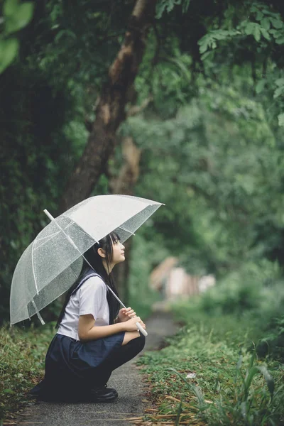 在雨中的自然人行道上坐着雨伞的亚洲学校女孩肖像 — 图库照片