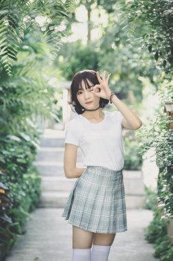 Beyaz gömlekli ve etekli Asyalı bir kızın portresi. Açık hava klasik film tarzına bakıyor.