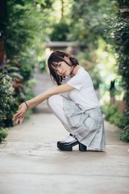 Beyaz gömlekli ve etekli Asyalı bir kızın portresi. Açık hava klasik film tarzına bakıyor.