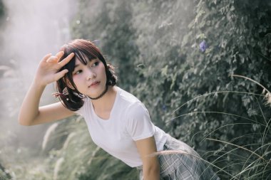 Beyaz gömlekli ve etekli Asyalı bir kızın portresi. Açık hava klasik film tarzına bakıyor.