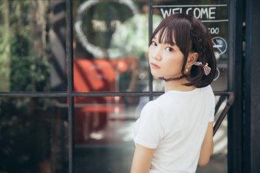 Beyaz gömlekli ve etekli Asyalı bir kızın portresi. Açık hava klasik film tarzına bakıyor.