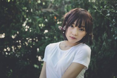 Beyaz gömlekli ve etekli Asyalı bir kızın portresi. Açık hava klasik film tarzına bakıyor.