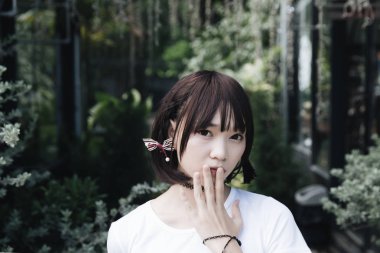 Beyaz gömlekli ve etekli Asyalı bir kızın portresi. Açık hava klasik film tarzına bakıyor.