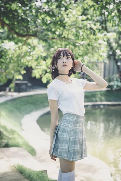 Beyaz gömlekli ve etekli Asyalı bir kızın portresi. Açık hava klasik film tarzına bakıyor.