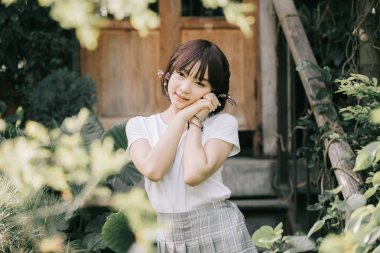 Beyaz gömlekli ve etekli Asyalı bir kızın portresi. Açık hava klasik film tarzına bakıyor.