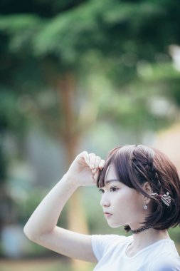 Beyaz gömlekli ve etekli Asyalı bir kızın portresi. Açık hava klasik film tarzına bakıyor.