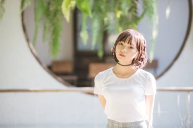 Beyaz gömlekli ve etekli Asyalı bir kızın portresi. Açık hava klasik film tarzına bakıyor.