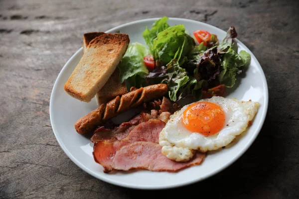 英語朝食揚げ卵 ソーセージ ベーコン サラダ 神秘的な光の中の木製の背景にトースト — ストック写真