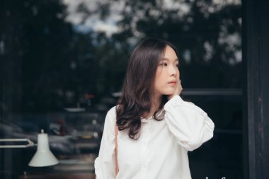 Açık şehir arka planında modern tarzda düşünen ve görünen genç bir kadın portresi.