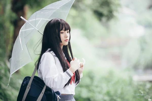 亚洲女学生的肖像看着自然人行道在下雨 — 图库照片