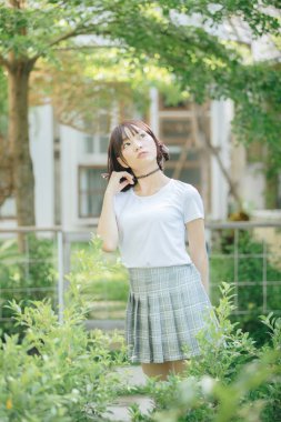 Beyaz gömlekli ve etekli Asyalı bir kızın portresi. Açık hava klasik film tarzına bakıyor.