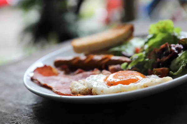 英語朝食揚げ卵 ソーセージ ベーコン サラダ 神秘的な光の中の木製の背景にトースト — ストック写真