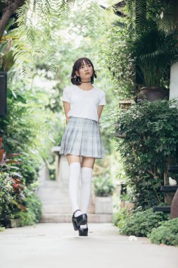 Beyaz gömlekli ve etekli Asyalı bir kızın portresi. Açık hava klasik film tarzına bakıyor.