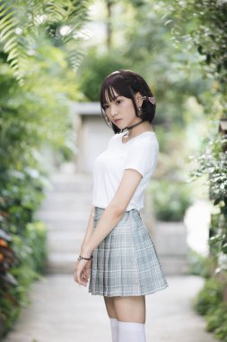 Beyaz gömlekli ve etekli Asyalı bir kızın portresi. Açık hava klasik film tarzına bakıyor.