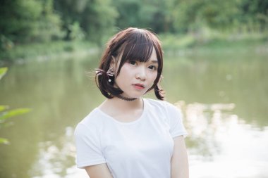 Beyaz gömlekli ve etekli Asyalı bir kızın portresi. Açık hava klasik film tarzına bakıyor.