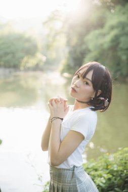 Beyaz gömlekli ve etekli Asyalı bir kızın portresi. Açık hava klasik film tarzına bakıyor.