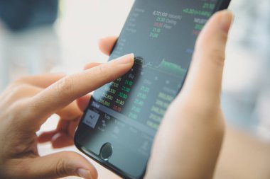 Akıllı telefon ile çalışan bir kadın kahve dükkanında hisse senedi ticareti, iş konsepti