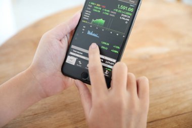 Akıllı telefon ile çalışan bir kadın kahve dükkanında hisse senedi ticareti, iş konsepti