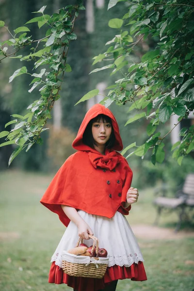 Retrato de mujer joven con traje de Caperucita Roja con manzana y pan en la cesta en fondo verde parque de árboles —  Fotos de Stock