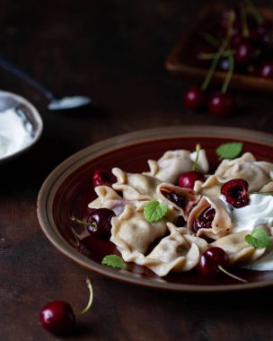 Kirazlı hamur tatlısı ve ekşi krema sosu tabakta, tek kesim, görünür malzemeler..