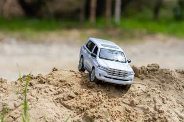 Oyuncak beyaz SUV kumun üzerinde, arka planda yeşil bitkiler var..