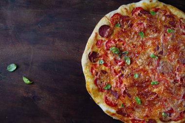 Kahverengi ahşap zemin üzerine fesleğen serpiştirilmiş füme sosisli pizza, boş alan..